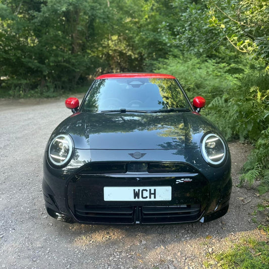Black Mini Cooper car with red top parked on a gravel road surrounded by greenery